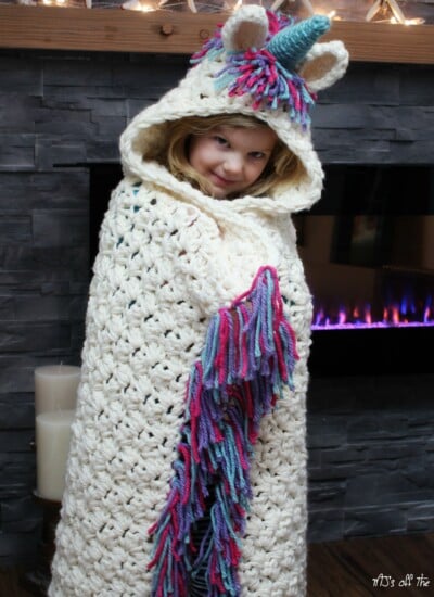 A little girl wearing a hoodie featuring a crocheted unicorn design.
