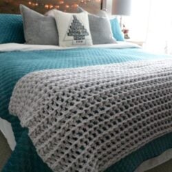 A bed with a bulky crocheted blanket on it.
