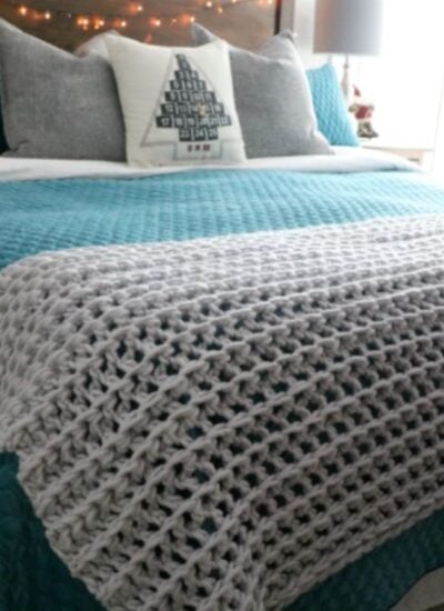 A bed with a bulky crocheted blanket on it.