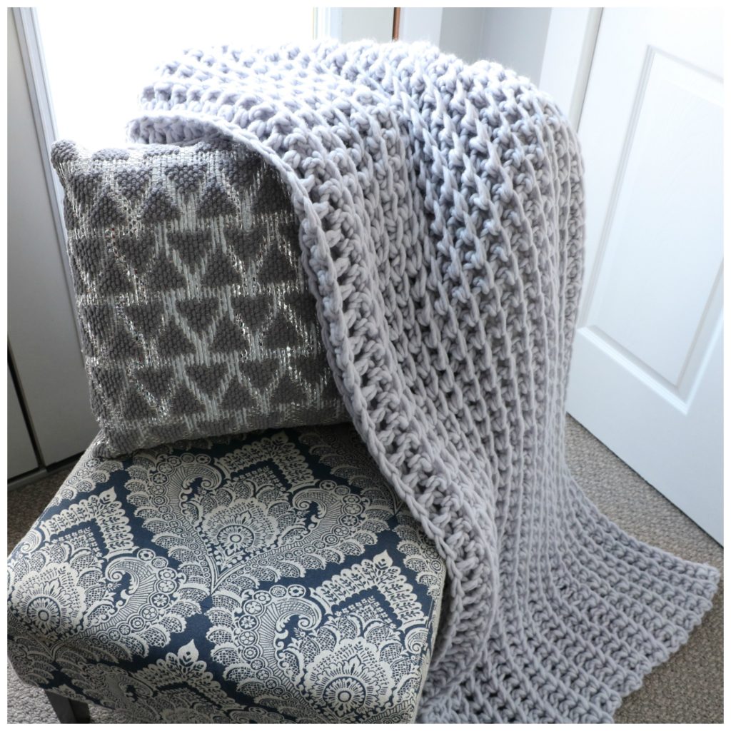 A bulky crocheted blanket sitting on a chair.