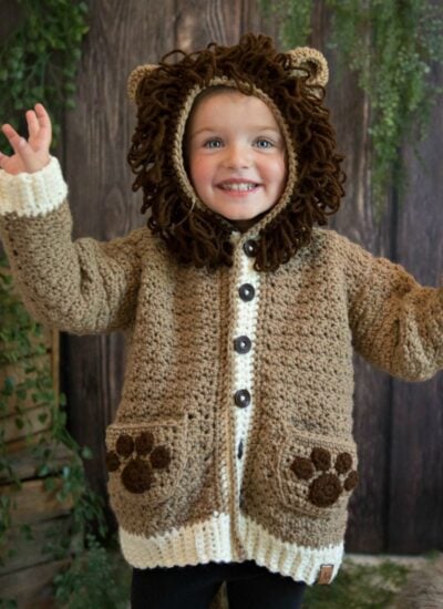 A little girl wearing a crocheted lion cardigan called "The Piece of Cake Cardi".