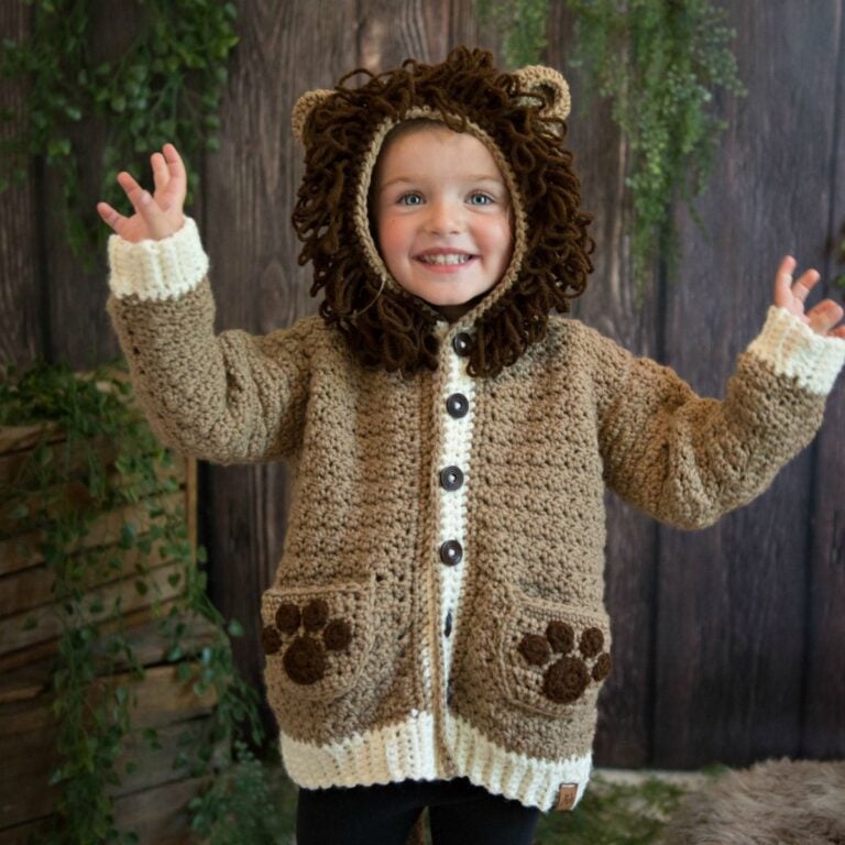 A little girl wearing a crocheted lion cardigan called "The Piece of Cake Cardi".