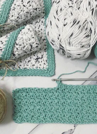 A Rustic Farmhouse crocheted blanket, yarn, and crochet hooks on a table.