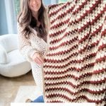 Woman holding a large crochet granny blanket with brown, cream, and rust stripes; text overlay reads "Fall for Granny Blanket Free Crochet Pattern & Video"—perfect paired with Crochet Rustic Farmhouse Pumpkins for cozy autumn décor.