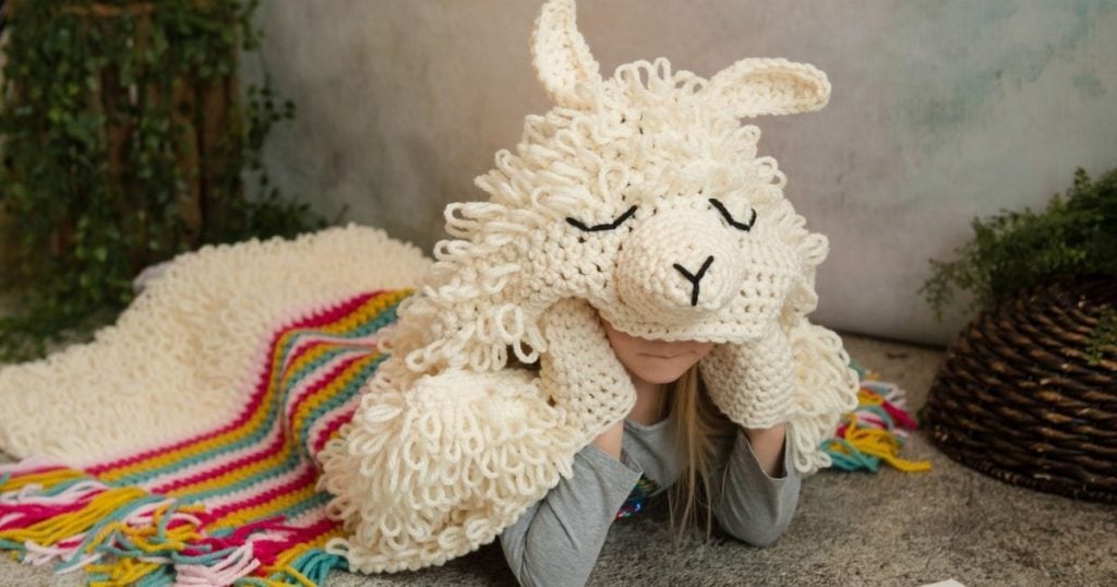 A girl laying on the ground with a crocheted alpaca my Llama Blanket.