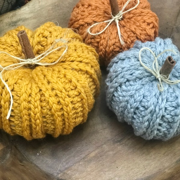 Three knitted rustic pumpkins on a wooden table.