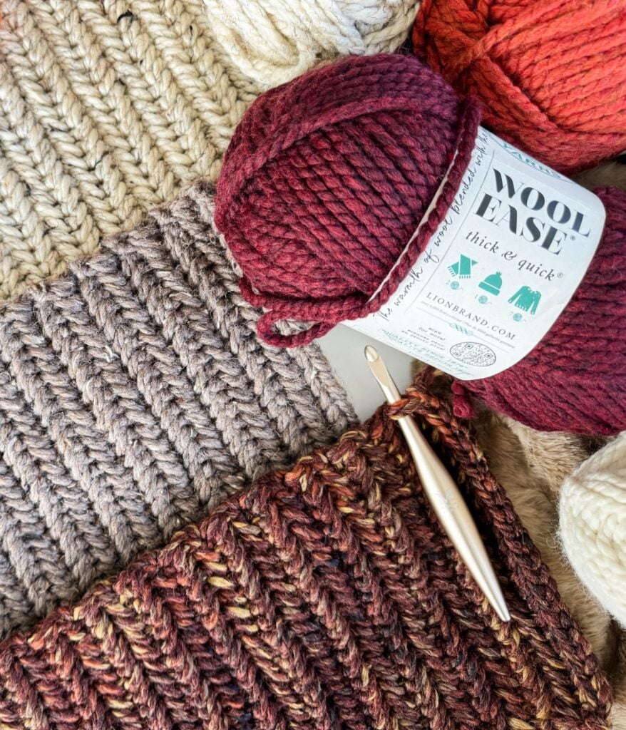 Several skeins of yarn, a crochet hook, and partially completed crochet projects are arranged on a surface, alongside a handy yarn substitution guide.