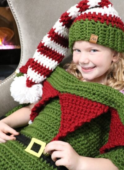 A little girl wearing a Christmas elf hat and scarf.