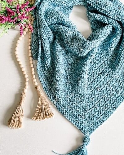 A blue crocheted scarf with tassels and flowers using the Herringbone Stitch crochet technique.
