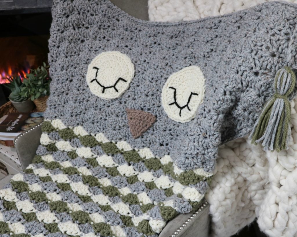 A Sleepy Owl Cocoon Blanket sitting on a chair next to a fireplace.