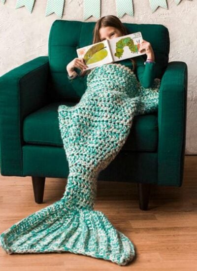 A girl reading a book while sitting in a chair with a bulky mermaid tail blanket.