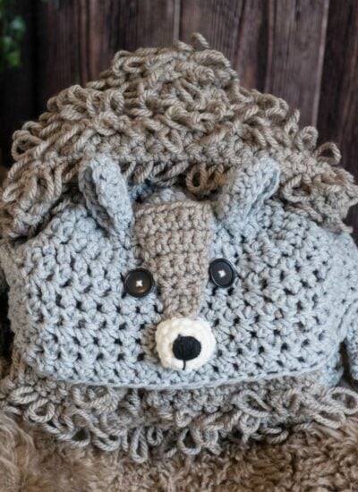 A crocheted hedgehog stuffed animal lying on a woodland squirrel blanket.