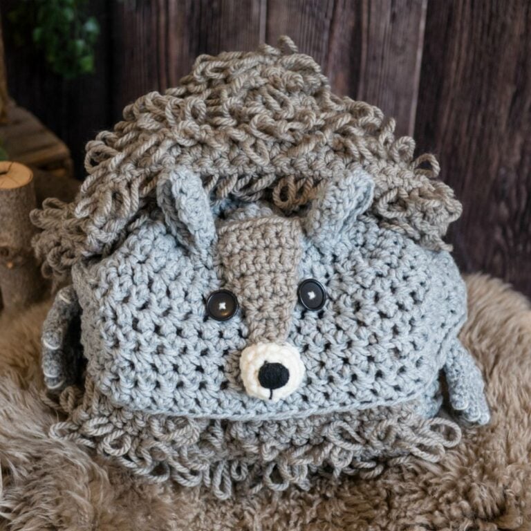 A crocheted hedgehog stuffed animal lying on a woodland squirrel blanket.