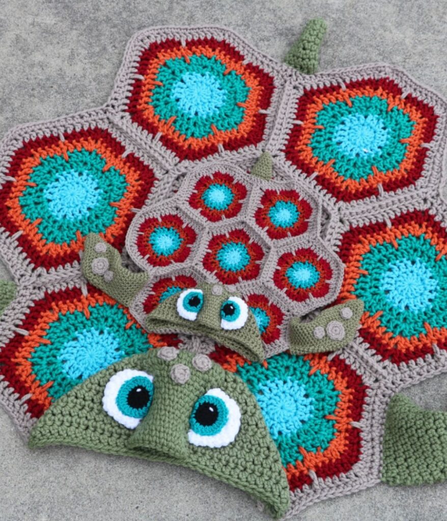A Hooded Sea Turtle Blanket and matching hat designed to look like a turtle, featuring hexagonal patterns in blue, red, and beige with cartoonish eyes.