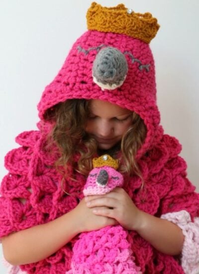 A little girl wearing a crocheted pink hooded flamingo hoodie.