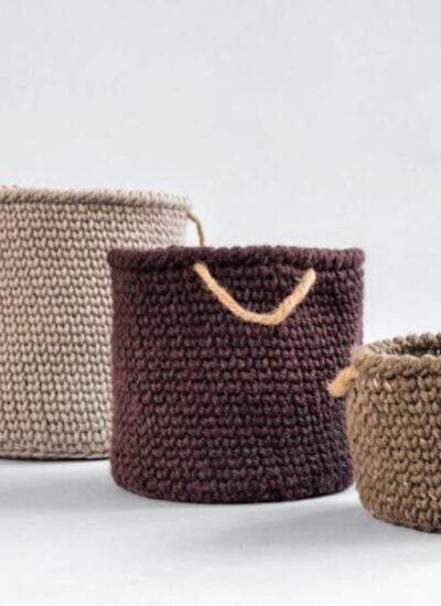 Three bulky knitted baskets with handles on a white surface.