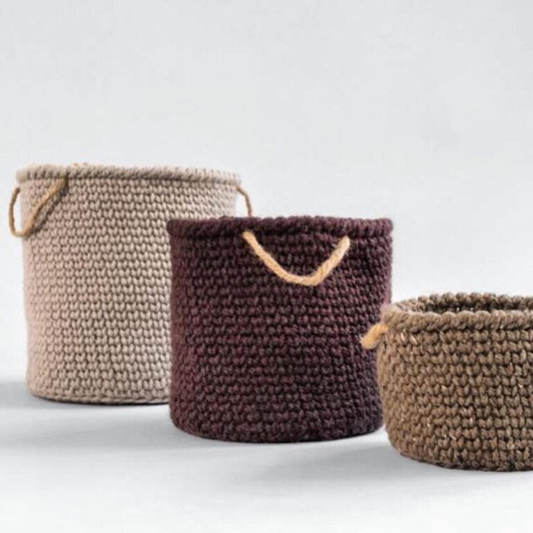 Three bulky knitted baskets with handles on a white surface.