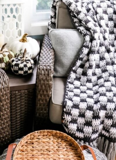 A bulky black and white blanket is sitting on a chair next to a wicker basket.