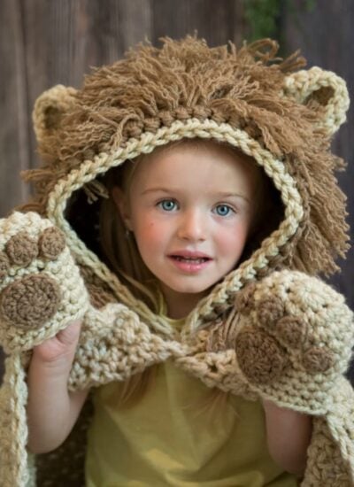 A little girl wearing a hooded lion blanket.