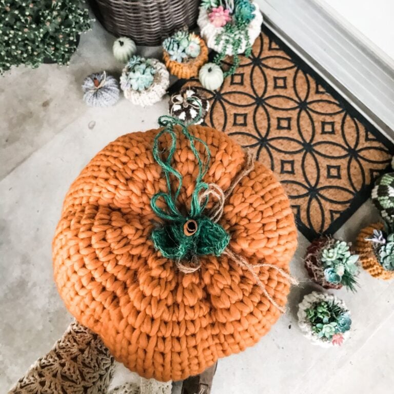 A person is holding a rustic knit pumpkin on a porch.