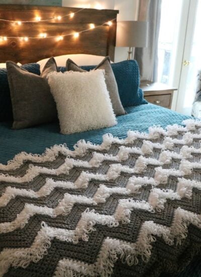 A bed with a loopy crocheted chevron blanket.