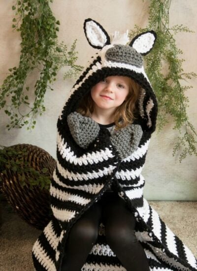 A little girl wearing a hooded zebra blanket.