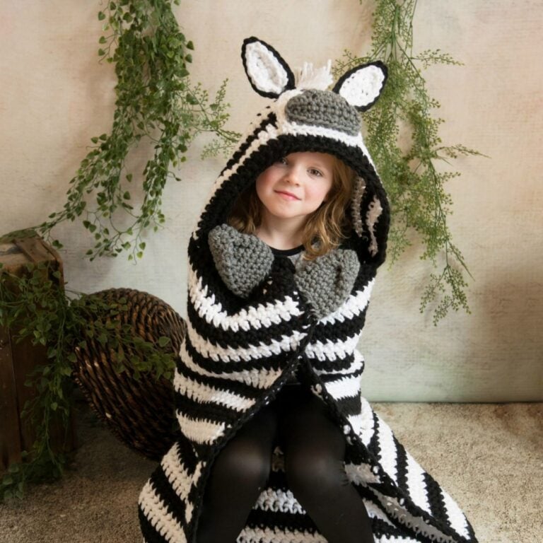 A little girl wearing a hooded zebra blanket.