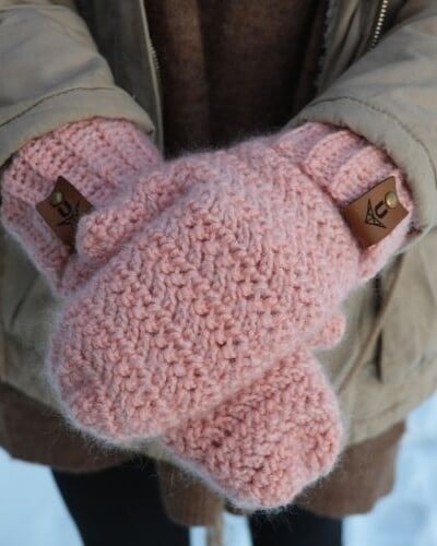 A woman experiencing winter bliss, adorned with pink knitted mittens while surrounded by snow.