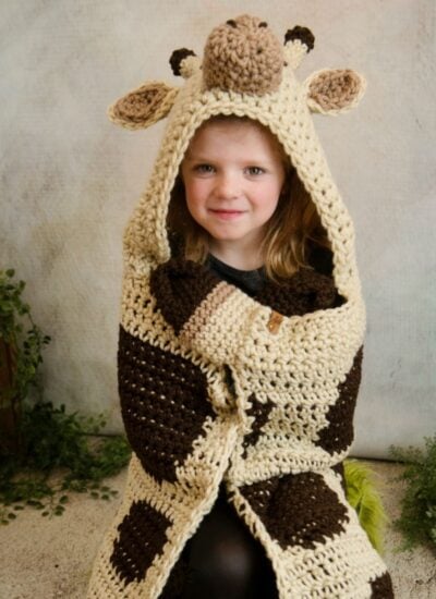 A little girl wearing a hooded giraffe blanket.