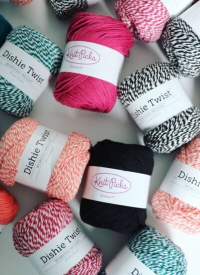 Assorted skeins of Knit Picks Dishie Twist yarn in vibrant shades—perfect for creating your own Dishie-lous Market Bag—are arranged in pink, black, white, teal, and coral on a flat surface.