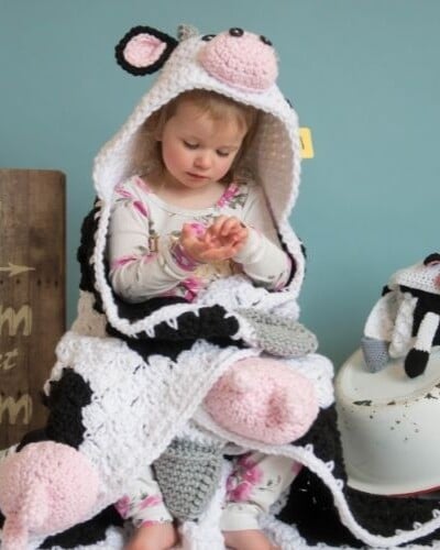 A little girl is sitting on a hooded cow blanket.