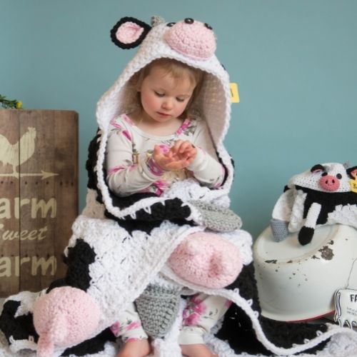 A little girl is sitting on a hooded cow blanket.