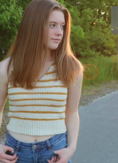 A girl in a striped tank top standing on the side of a road at sunset.