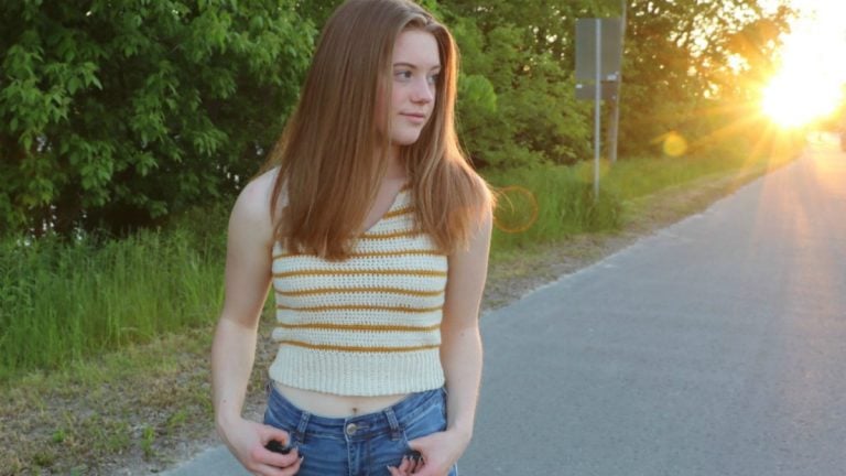 A girl in a striped tank top standing on the side of a road at sunset.