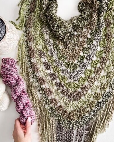 A hand delicately clasping a crocheted pistachio wrap, intertwined with yarn.