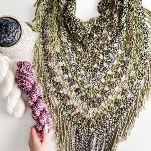 A hand delicately clasping a crocheted pistachio wrap, intertwined with yarn.