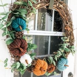 A crochet pumpkin wreath hangs on a front door.