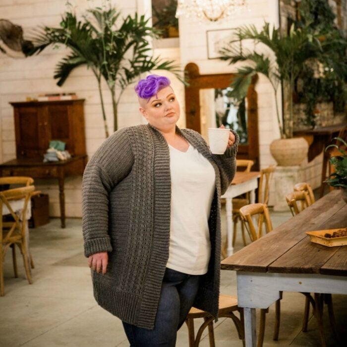 A woman in a cardigan standing in front of a table.