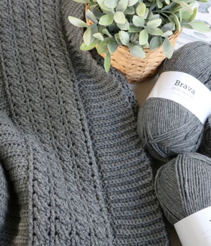 A grey knitted blanket and yarn, perfect for a cozy cable cardigan project, displayed on a table.