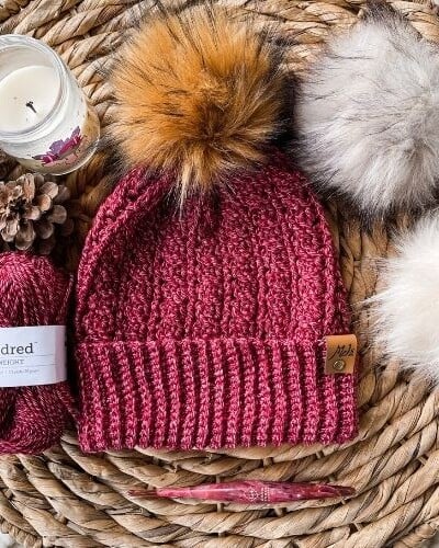 A knitted beanie with pom poms on a wicker basket.