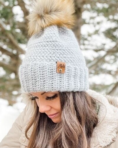 A woman wearing a gray beanie with a pom-pom, showcasing a stylish and cozy accessory.