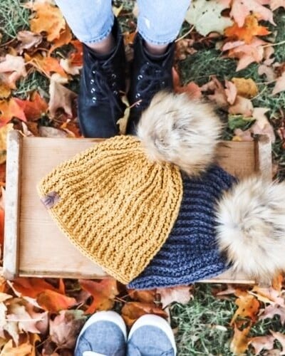 Two people sitting on a wooden tray with crochet baby hat pattern.