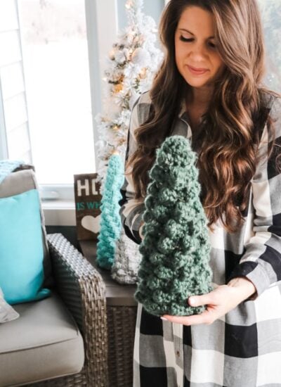 A woman holding a crocheted Christmas sweater tree.