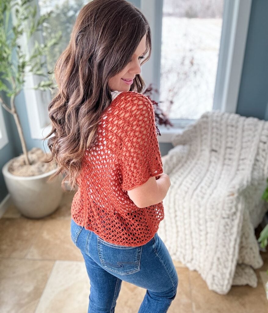 Woman in a Rusty Road crop top and blue jeans standing in a room with a snowy view outside, looking over her shoulder.