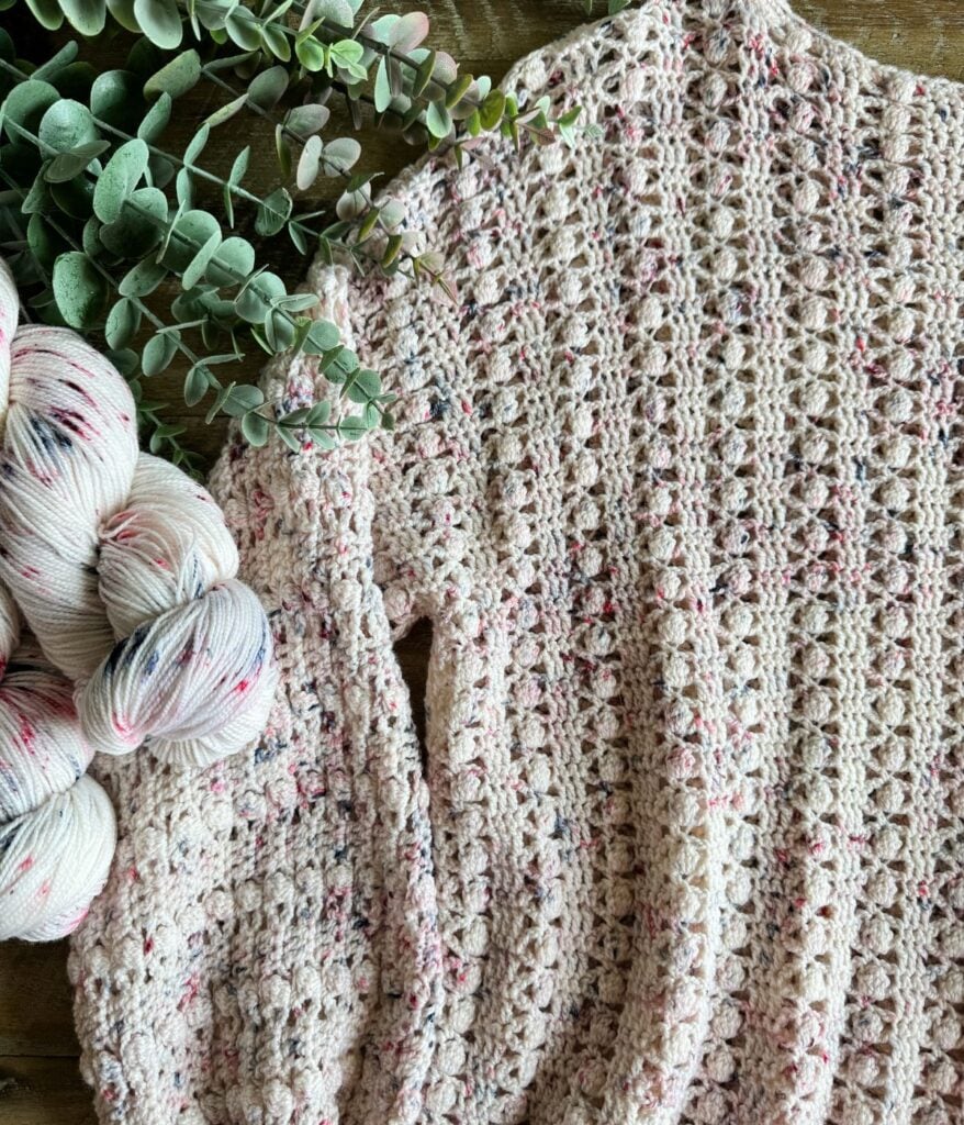 Handmade Gum Drop Pullover crochet blanket with variegated yarn and accompanying skeins on a wooden surface.