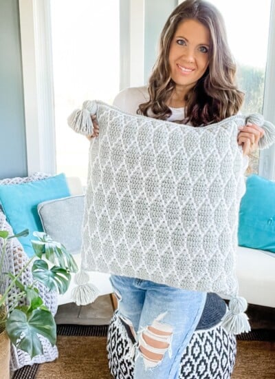 A woman holding up a Surfside mosaic pillow in a living room.