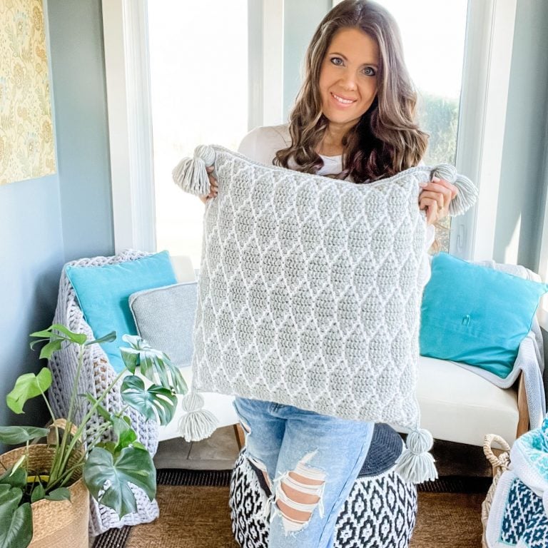 A woman holding up a Surfside mosaic pillow in a living room.