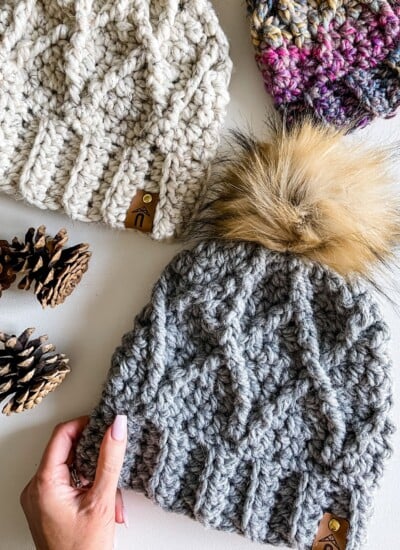 Tuff Love Crochet Toque is a stylish hat adorned with pom poms and pine cones.