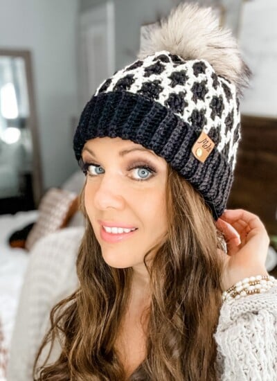A woman donning a modish crochet hat with a mosaic pattern and a pom pom.