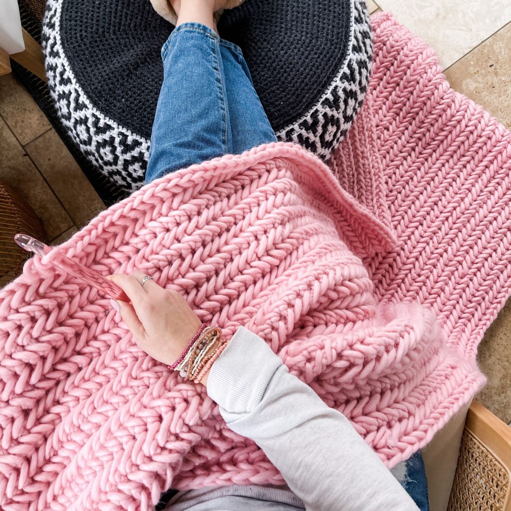 pink crochet blanket on lap of woman crochetring